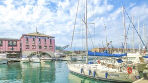 Un port de plaisance avec plusieurs bateaux amarrés, un bâtiment rose et un ciel dégagé.