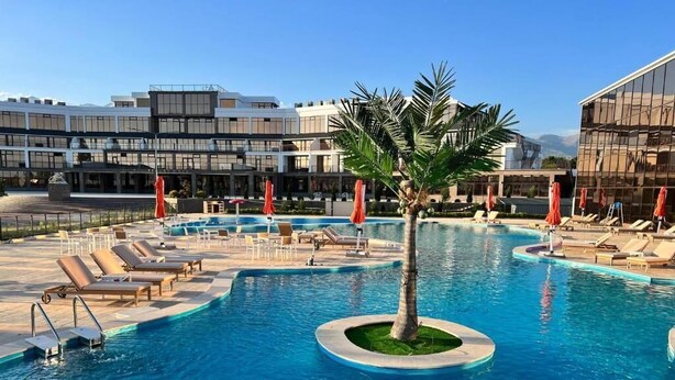 A pool area with lounge chairs and umbrellas, surrounded by modern buildings. - Baytur Resort & Spa (Cholpon-Ata)