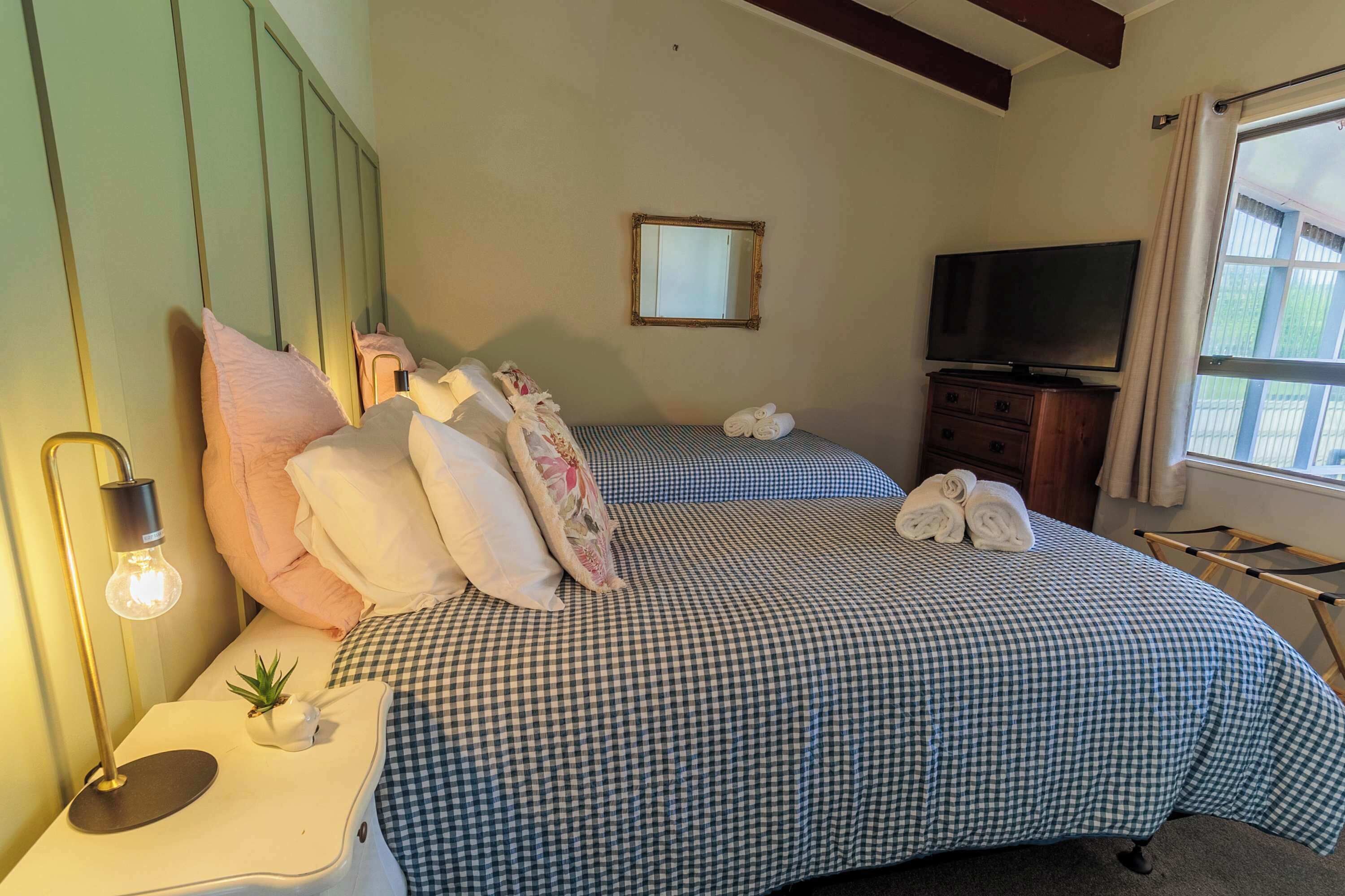 Quarto de hotel com duas camas, televisão, espelho e janela com cortinas.