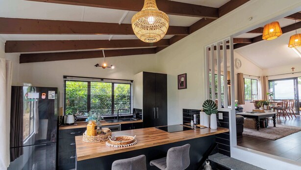 A modern kitchen with a wooden island, black cabinets, and a large window. - Cozy Lake Retreat - Games Room, Spa, Sleeps 6 (Hamurana)