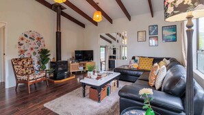 A living room with a fireplace, a sofa, a coffee table, and a television. - Cozy Lake Retreat - Games Room, Spa, Sleeps 6 (Hamurana)
