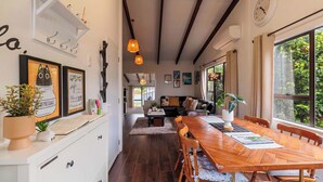 A dining area with a wooden table and chairs, a white cabinet with drawers, and a hanging light fixture. - Cozy Lake Retreat - Games Room, Spa, Sleeps 6 (Hamurana)