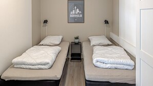 A small, clean room with two single beds, a nightstand with a lamp, and a framed cityscape picture on the wall. - Lovely apartment in Nexø with WiFi (Nexø)