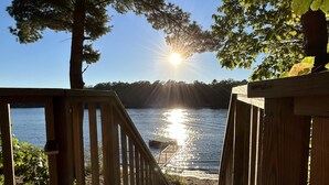 En træterrasse der fører ned til en sø, med udsigt til solnedgangen over vandet.