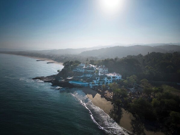 Una propiedad costera con playa, piscina y montañas al fondo.