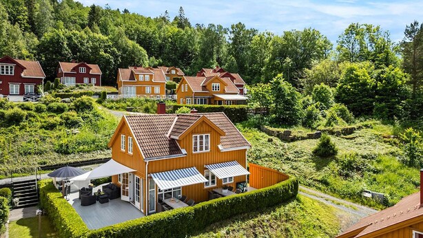 A cluster of wooden houses with sloped roofs, surrounded by lush greenery and hills.