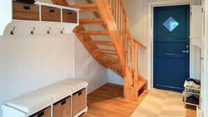 A wooden staircase leading to a dark blue door, white wall-mounted shelves with baskets, and a bench with storage baskets.