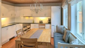 A modern kitchen with white cabinets, a wooden dining table, and a built-in seating area with cushions.