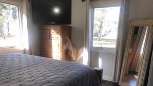 Ein Schlafzimmer mit einem großen Bett, einem Holzkasten, einem Flachbildfernseher und einem Spiegel.
