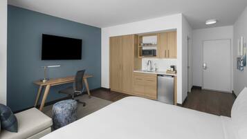 Een kleine hotelkamer met een bed, een bureau, een stoel, een kitchenette en een televisie.