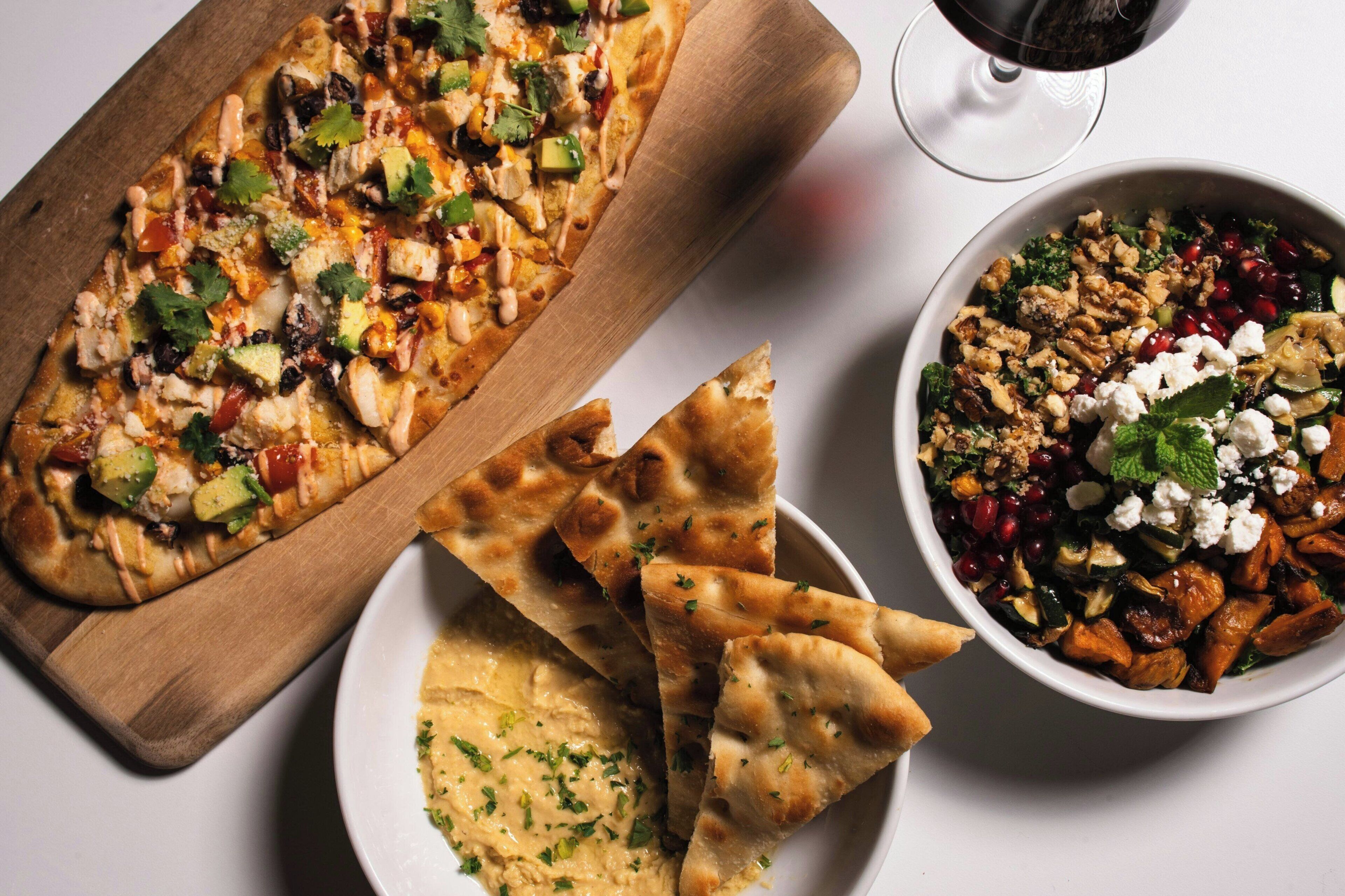 A meal with a flatbread, a bowl of salad, and a glass of red wine.