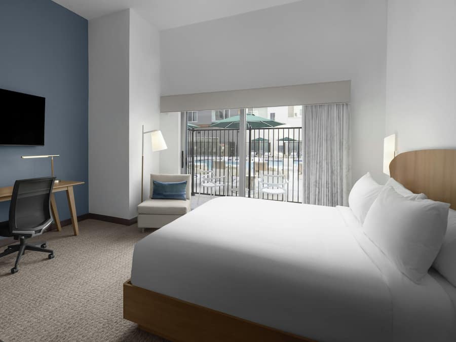 Une chambre d’hôtel équipée d’un lit, d’un bureau, d’une chaise et offrant une vue sur l’espace piscine.