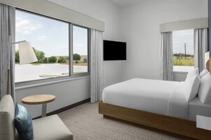 A hotel room with a bed, a TV, a small table, and a window with curtains.