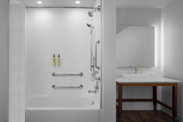 A modern bathroom with a white bathtub, shower, and sink, wooden floor, and a mirror above the sink. - Element by Marriott North Austin Tech Ridge (Austin)