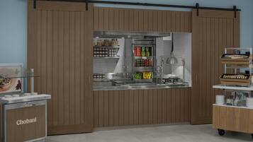 Una kitchenette con un refrigerador Chobani, una cafetera y un expositor de alimentos con diversos productos.