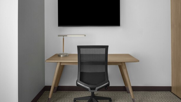 Ein Arbeitsplatz mit Schreibtisch, Stuhl und Wandfernseher.