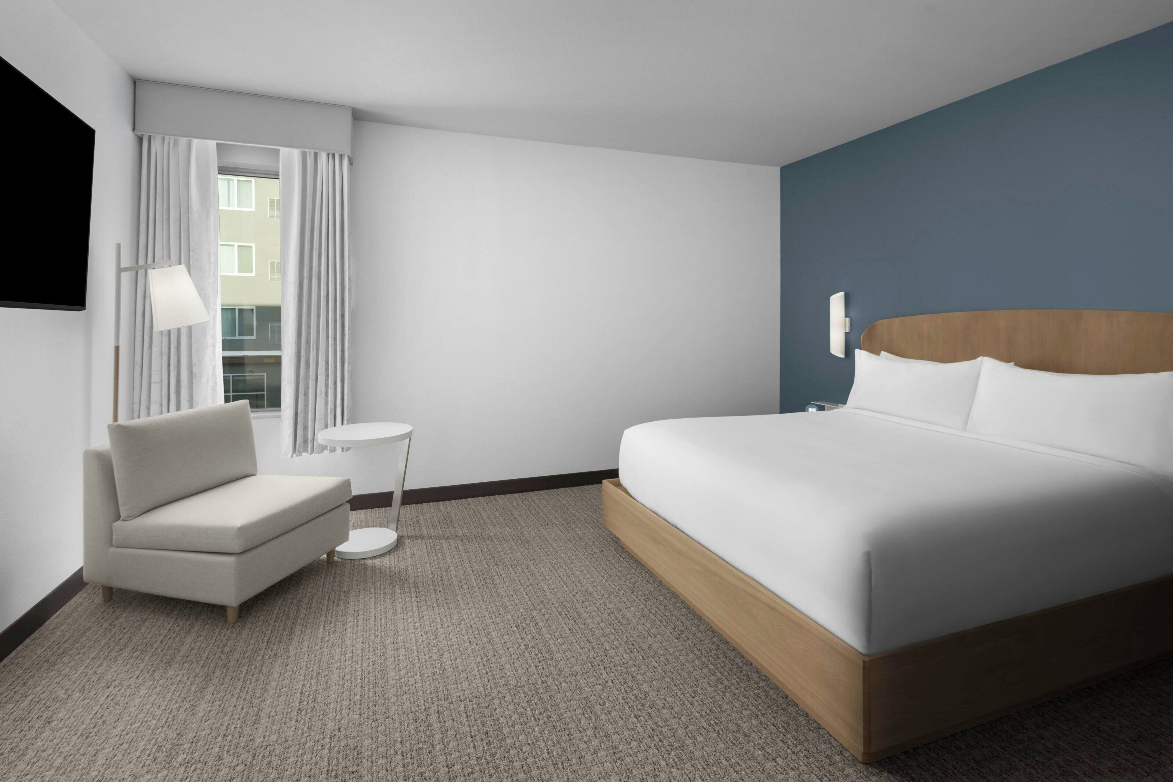 Habitación de hotel con cama, una silla, una mesita y ventana con cortinas.