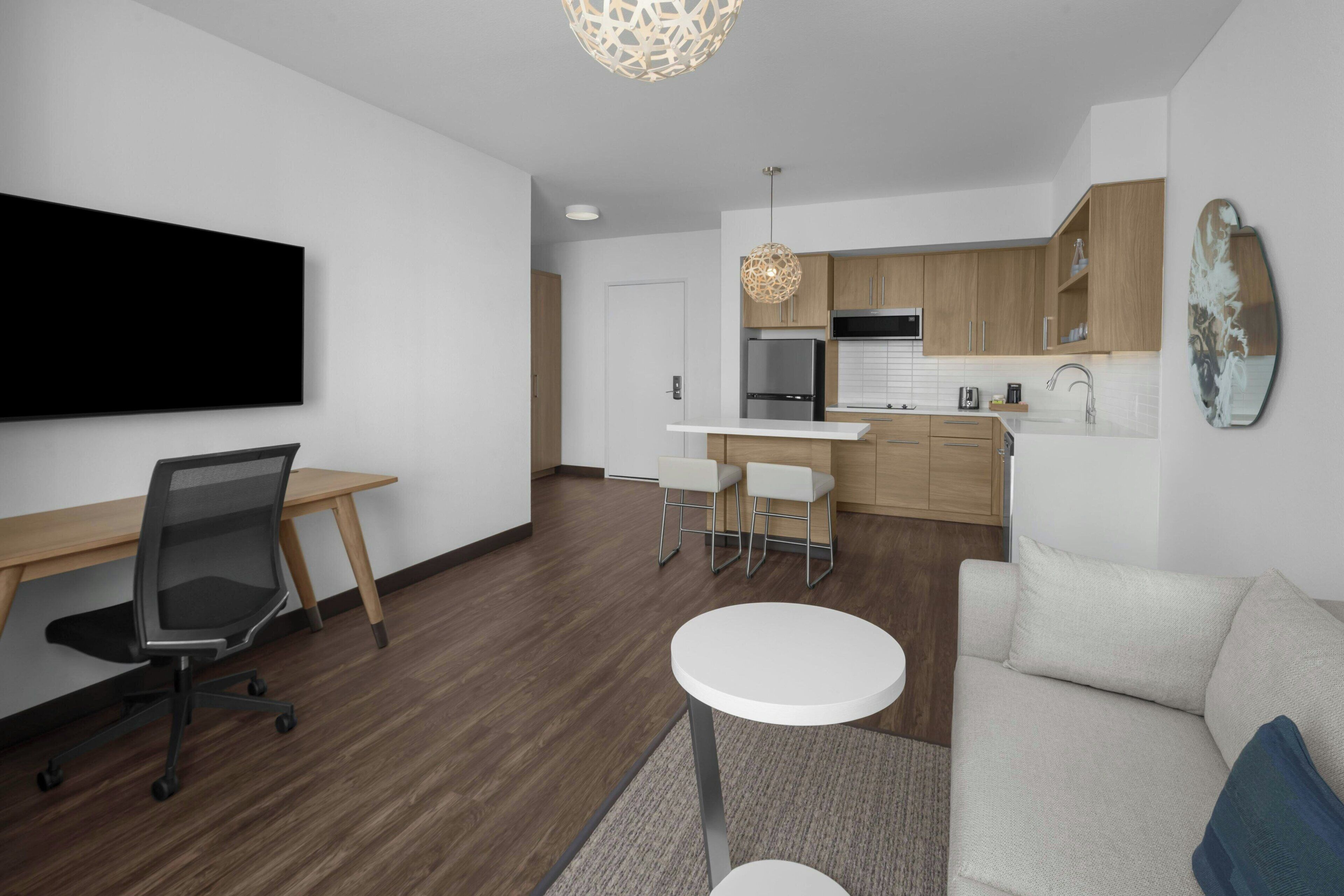A modern living room with a flat-screen TV, a sofa, a coffee table, and a dining area with a kitchen in the background.