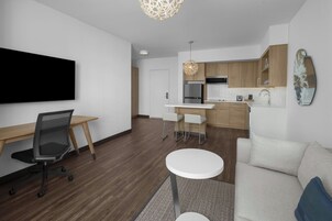 A modern living room with a flat-screen TV, a sofa, a coffee table, and a dining area with a kitchen in the background.
