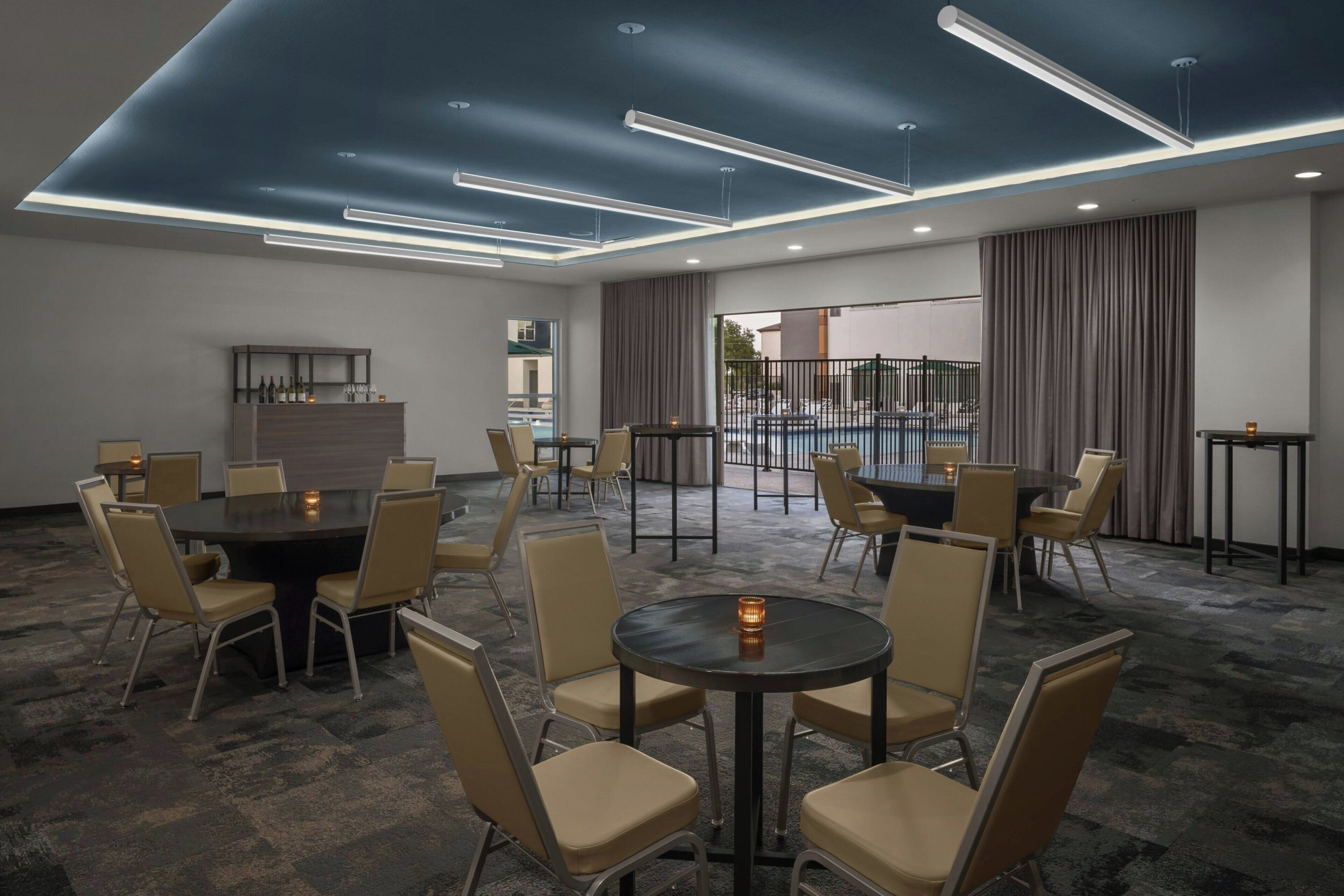 A conference room with multiple tables and chairs, a bar area, and a view of an outdoor pool.