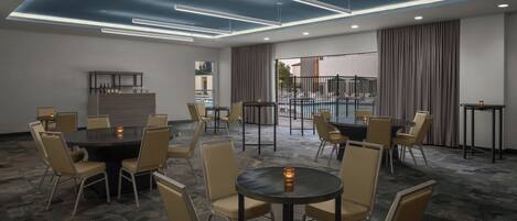A conference room with multiple tables and chairs, a bar area, and a view of an outdoor pool.