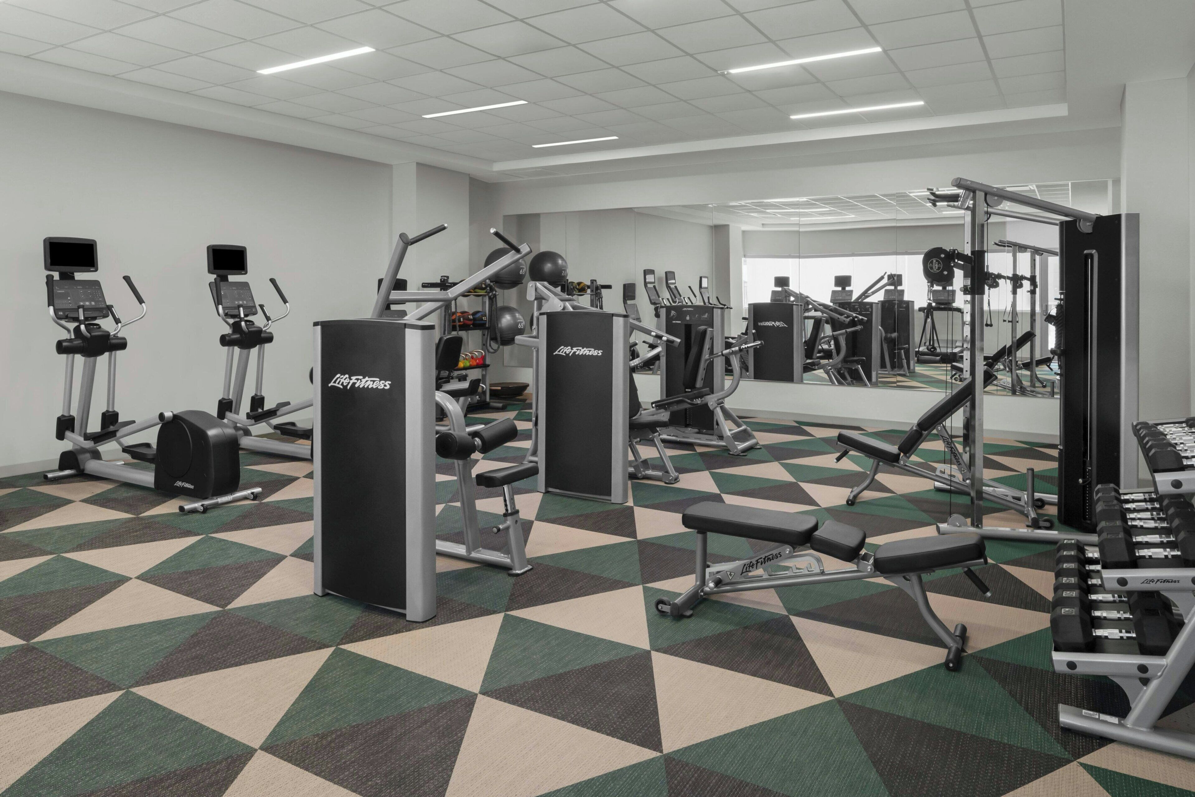 Et fitnesscenter med forskellig træningsudstyr, herunder løbebånd, styrkemaskiner og håndvægte.