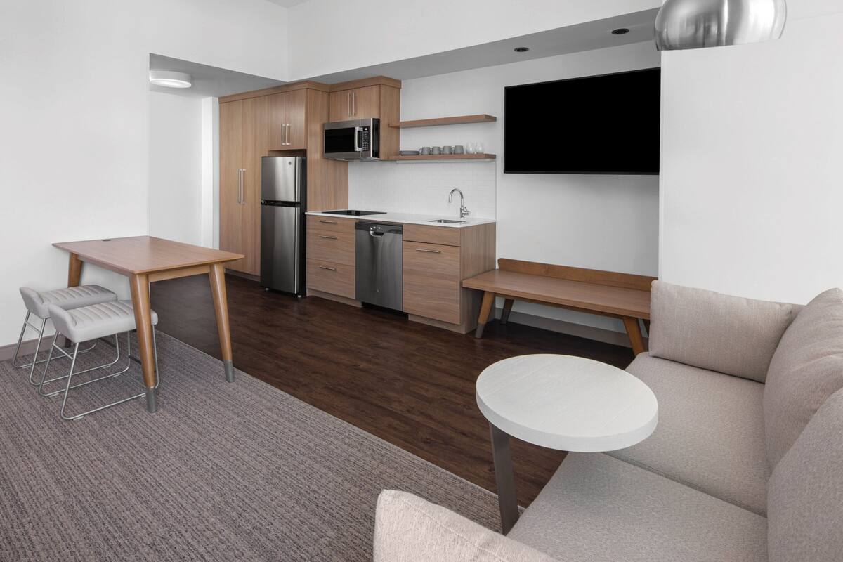 A modern kitchen with wooden cabinets, stainless steel appliances, and a flat-screen TV mounted on the wall.