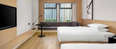 Ein modernes Hotelzimmer mit einem großen Bett, einer Couch, einem Fernseher und einem Fenster mit Blick auf die Stadt.