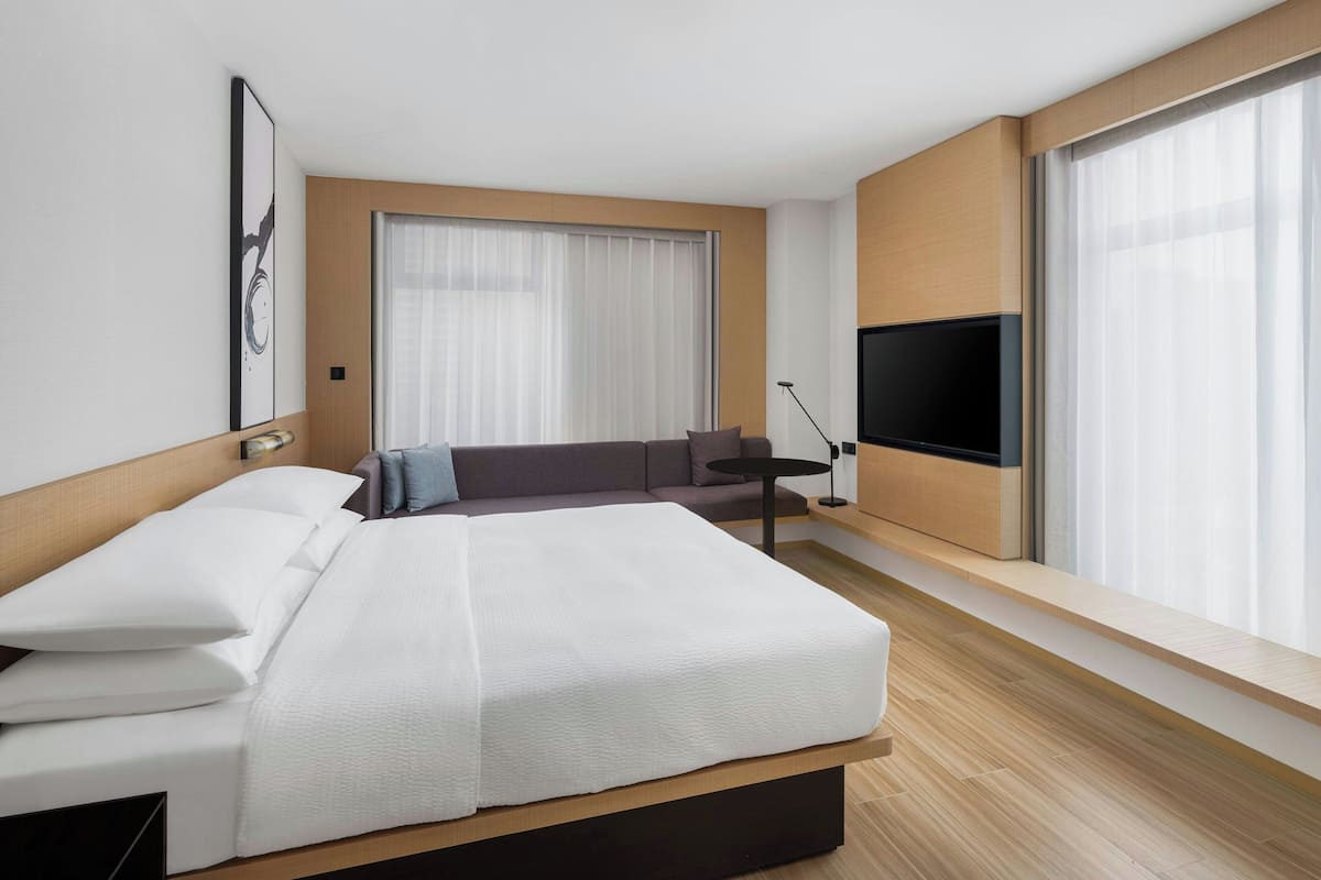 Une chambre d’hôtel moderne avec un grand lit, un canapé, une télévision et une fenêtre avec des rideaux.