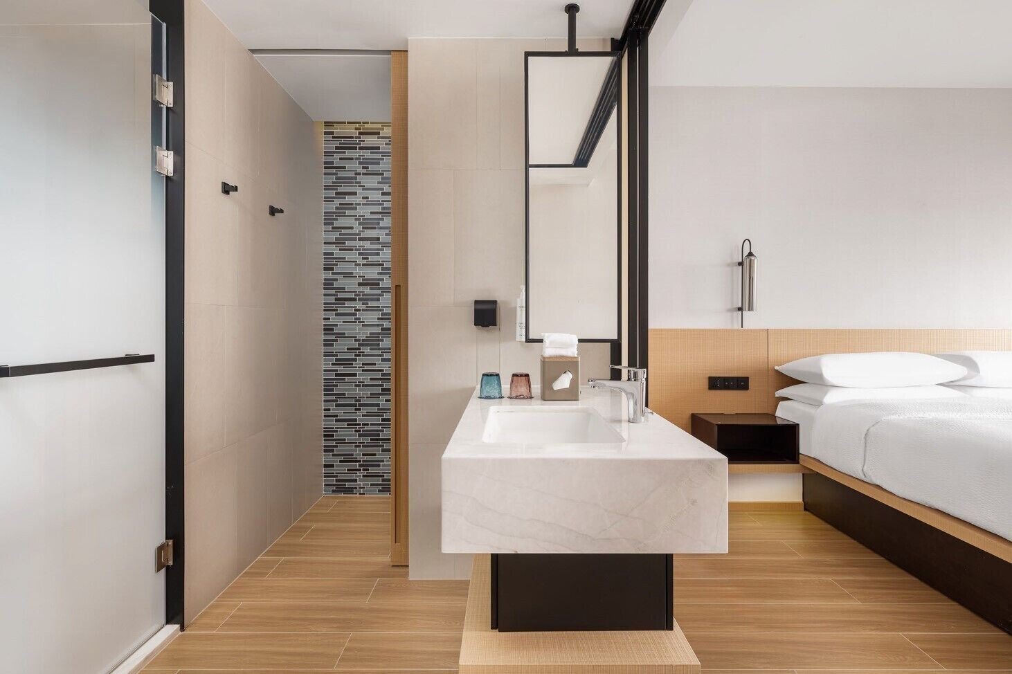 A modern hotel room with a large bed, a marble bathroom sink, and a wooden floor.