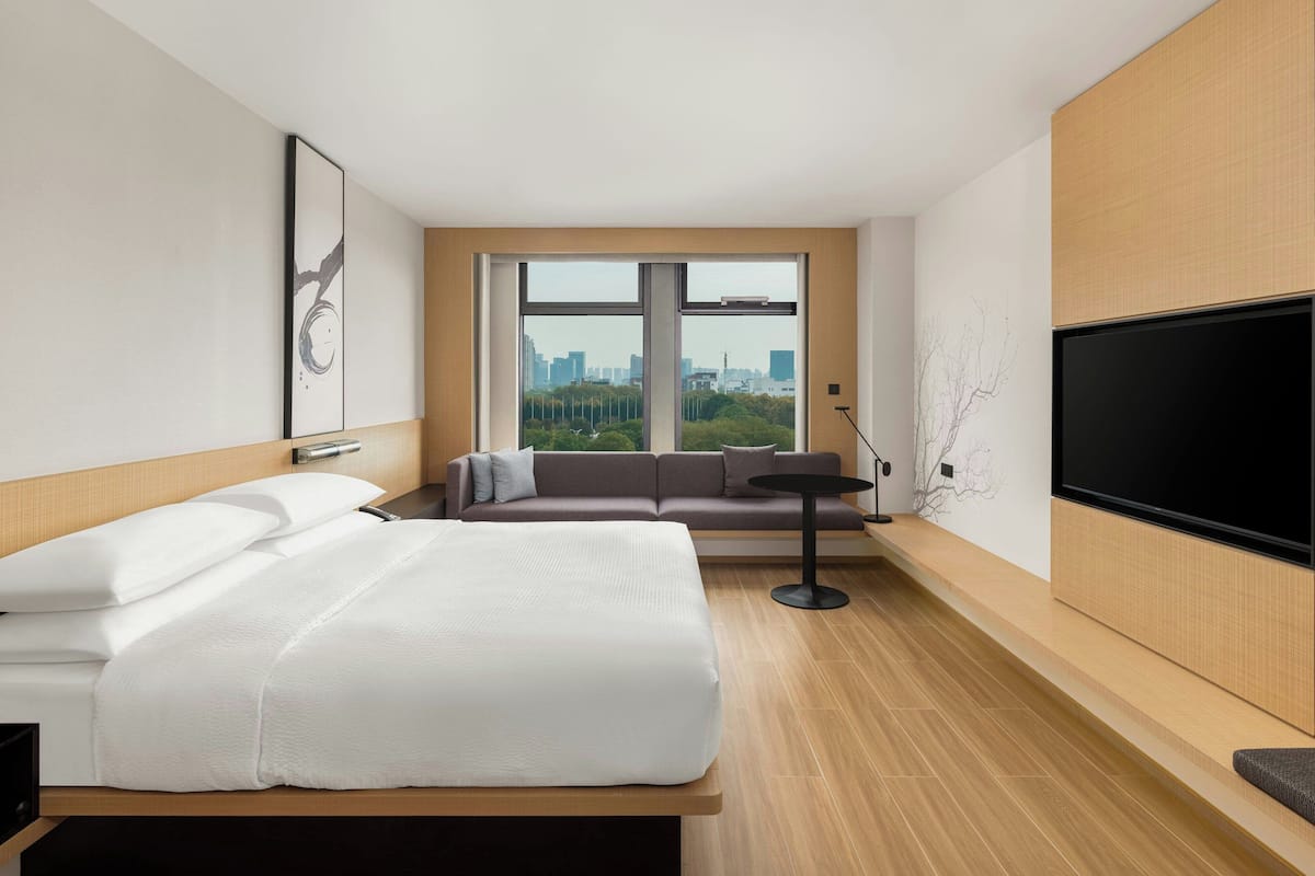 Une chambre d’hôtel moderne équipée d’un lit, d’un canapé, d’une télévision et d’une grande fenêtre donnant sur la ville.