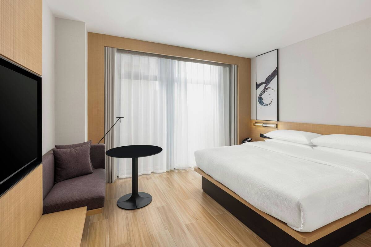 Une chambre d’hôtel moderne dotée d’un grand lit, d’un coin salon, d’une télévision et d’une fenêtre avec des rideaux.