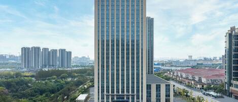 A tall, modern skyscraper with a glass facade, surrounded by greenery and other buildings.