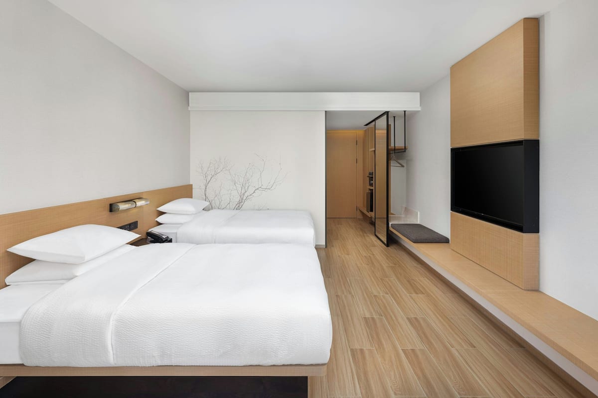 Une chambre d’hôtel moderne avec un grand lit, un téléviseur fixé au mur et un plancher en bois.