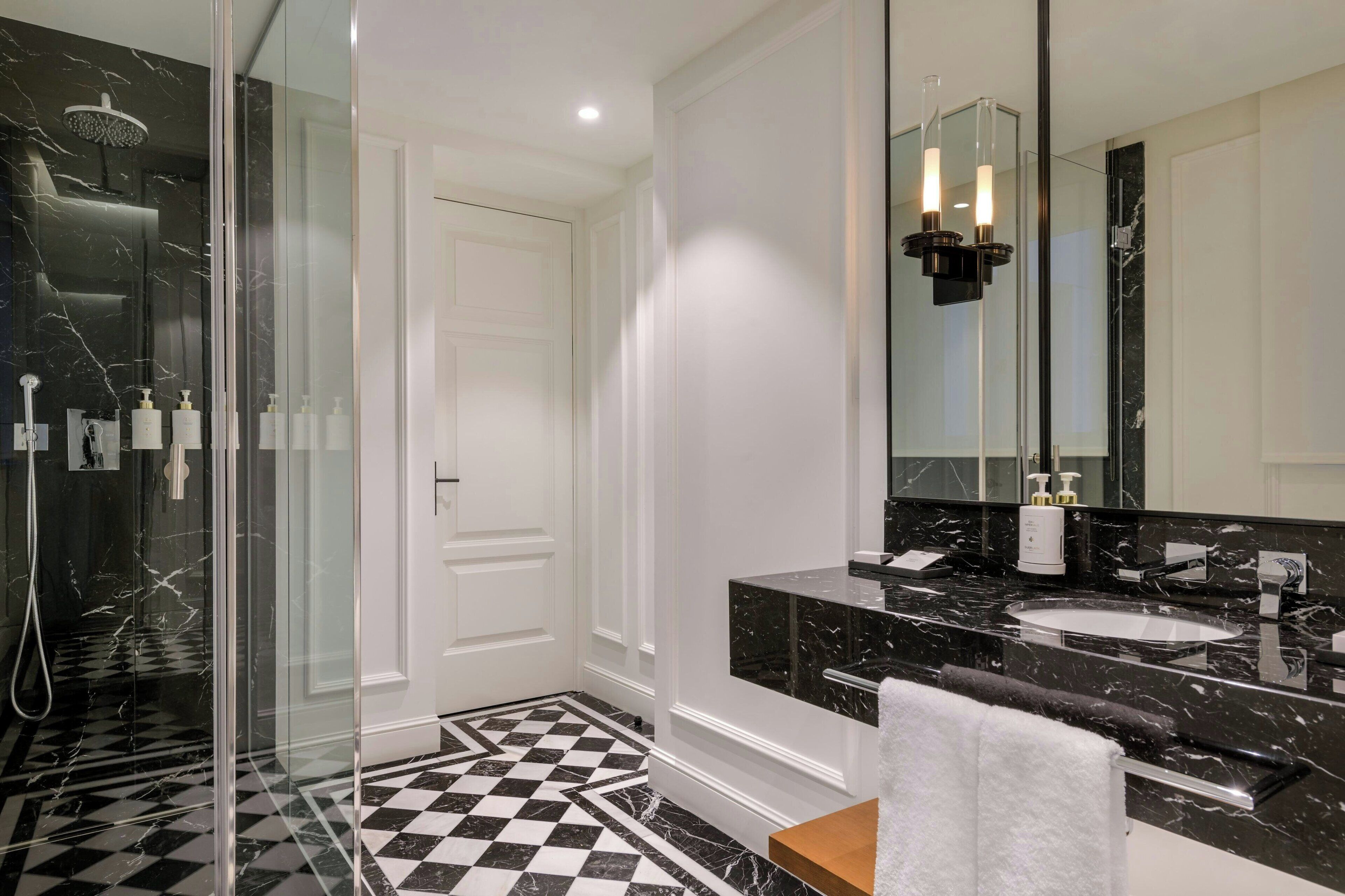 A modern bathroom with a glass-enclosed shower, a large mirror, and a black and white checkered floor.