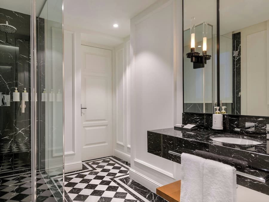 Un baño moderno con ducha envuelta en vidrio, un espejo grande y un suelo a cuadros blanco y negro.
