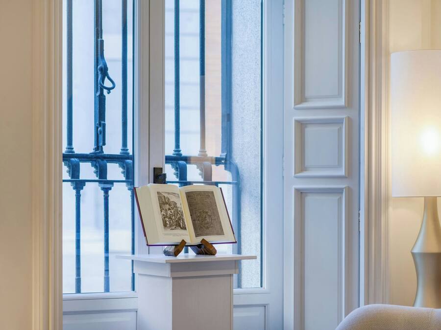 A room with a window, a book on a pedestal, and a lamp.