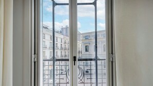 Vista a través de una ventana con barandilla metálica, que muestra una hilera de edificios con balcones.
