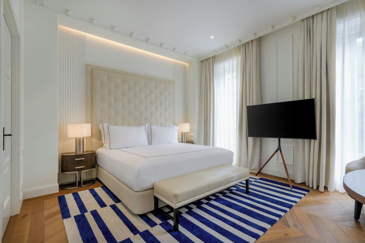 A modern hotel room with a large bed, a flat-screen TV, a bench, and a striped rug.