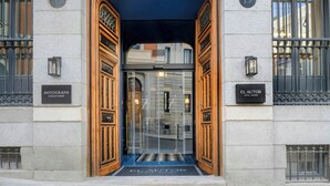 Entrada de un hotel con puerta de madera, paneles de vidrio y un felpudo negro.