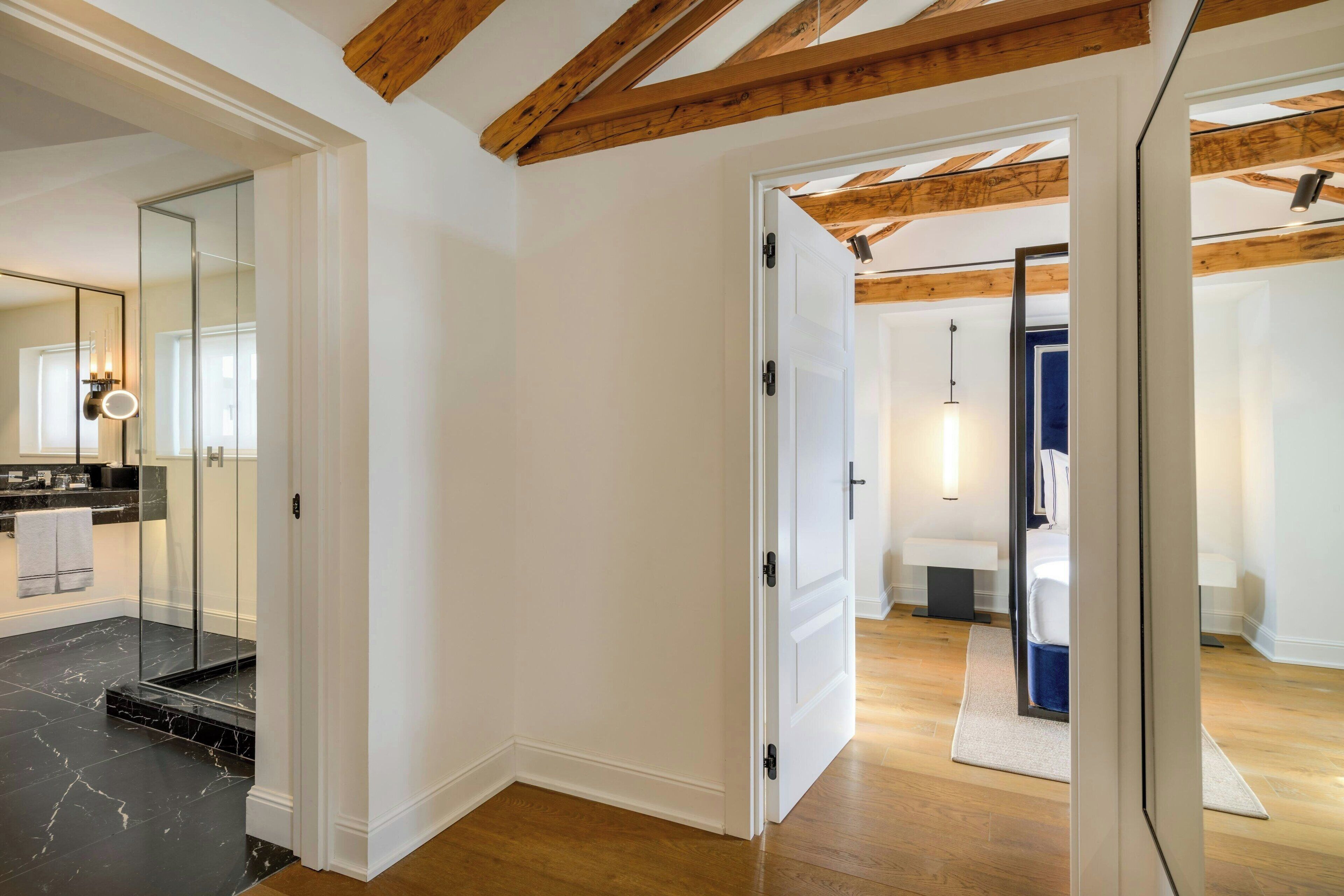 A modern bathroom with a glass shower enclosure, a white door, and wooden beams on the ceiling.