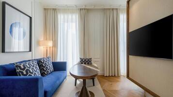 A modern living room with a blue sofa, a round table, and a flat-screen TV mounted on the wall.