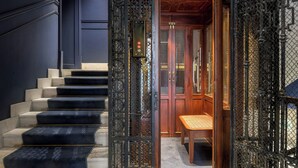 Una escalera con escalones negros que conduce a una puerta de madera con detalles de metalurgia intrincada.