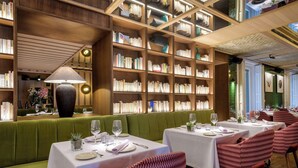 Un restaurante con estanterías de madera, asientos tapizados en verde y mesas dispuestas para comer.
