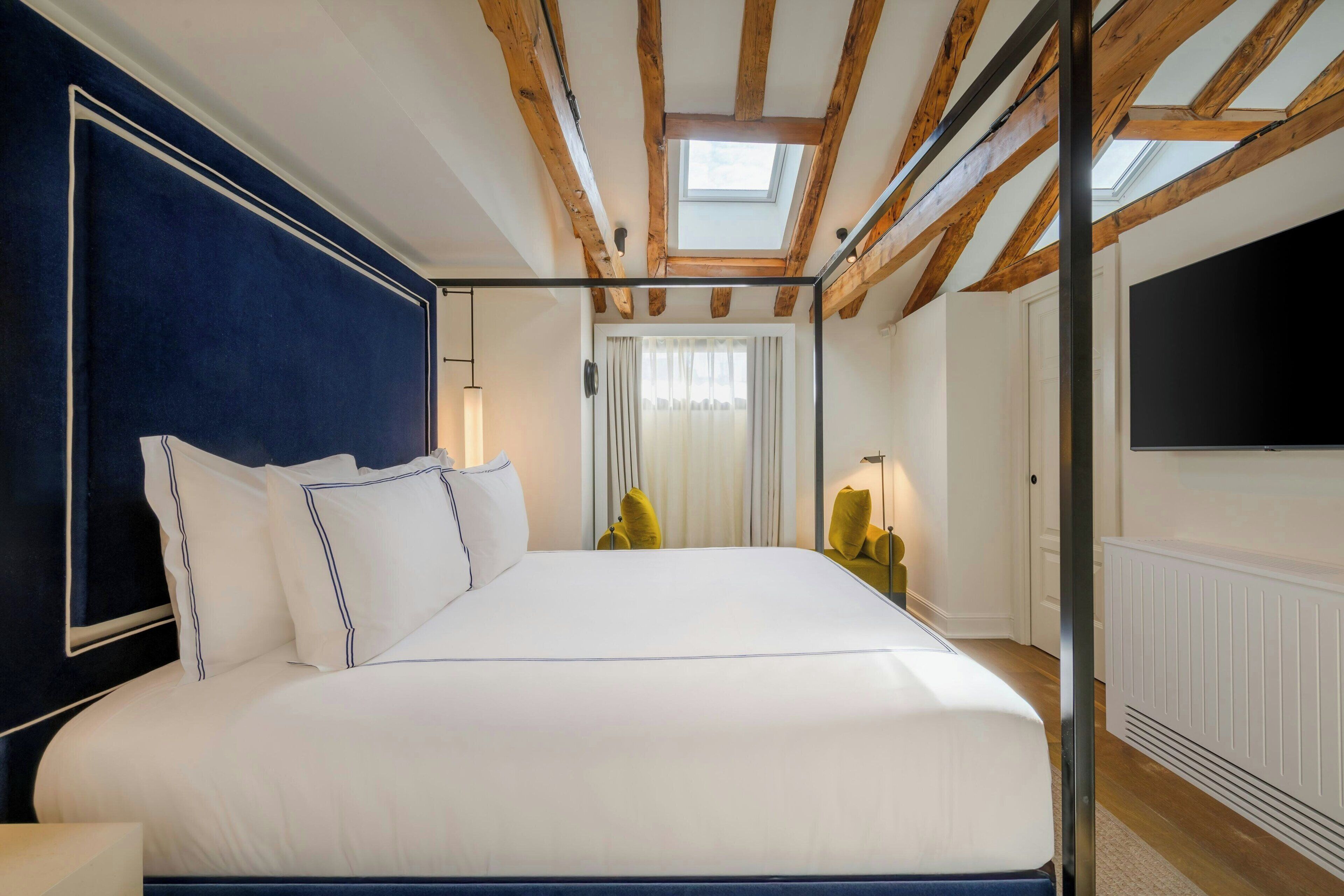 Un dormitorio con una cama grande, vigas de madera, un tragaluz, un televisor y un radiador.