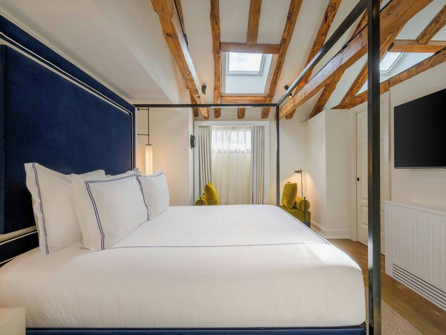 Un dormitorio con una cama grande, vigas de madera, un tragaluz, un televisor y un radiador.
