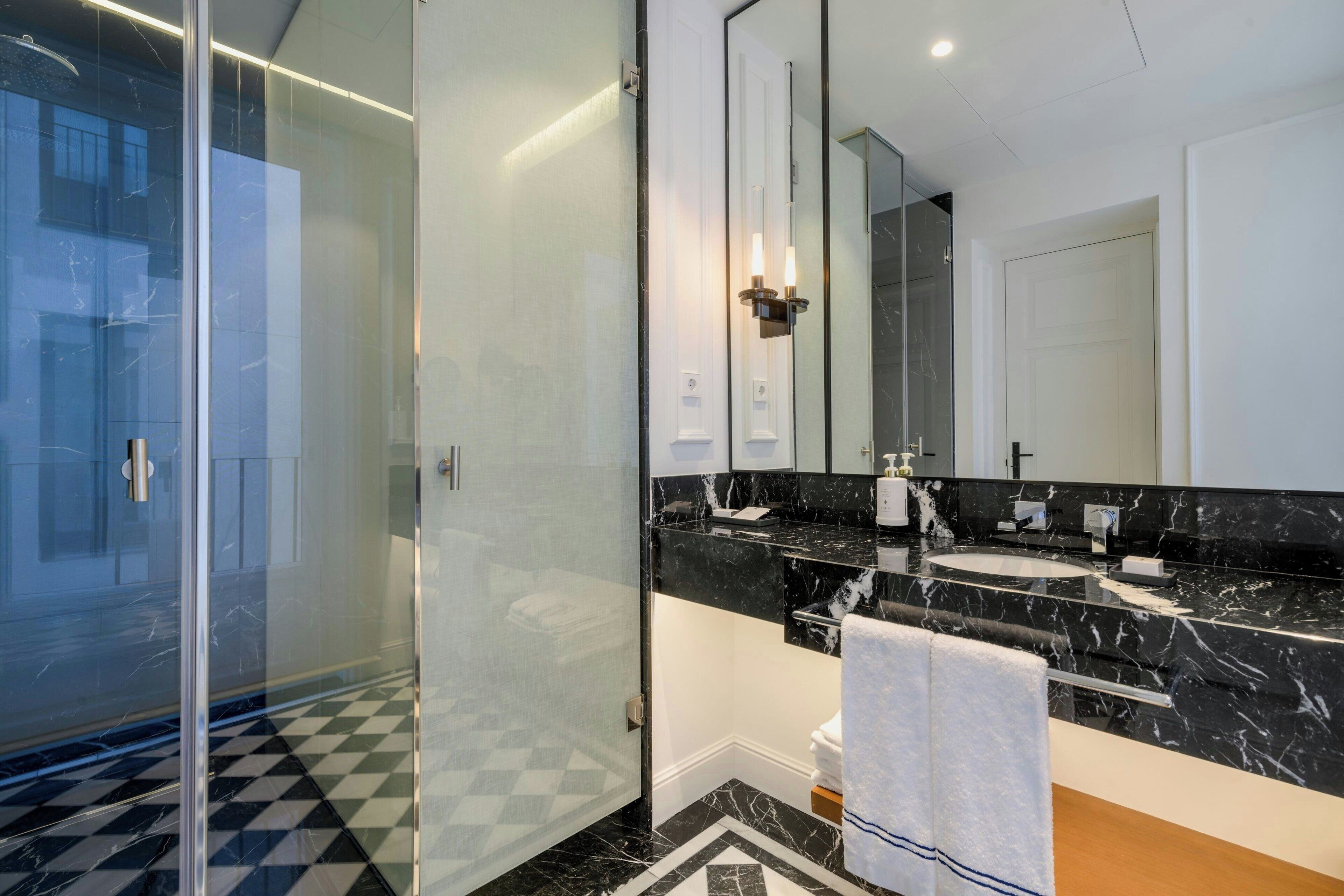 A modern bathroom with a glass shower enclosure, a black marble countertop, and a large mirror.