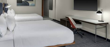 A hotel room with two beds, a desk, a chair, a TV, and artwork on the walls.