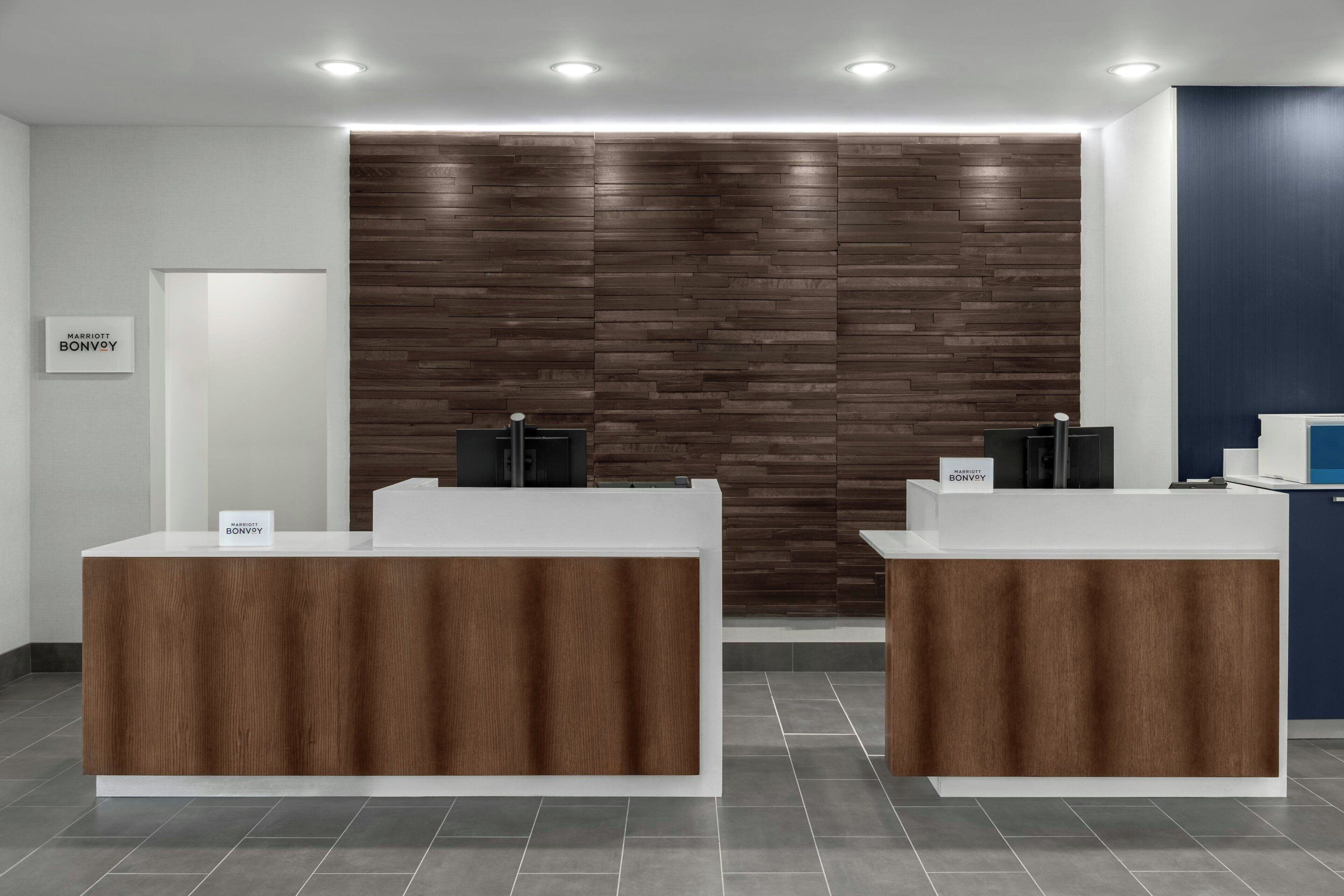 A reception area with two reception desks, a wooden wall, and a sign for Marriott Bonvoy.