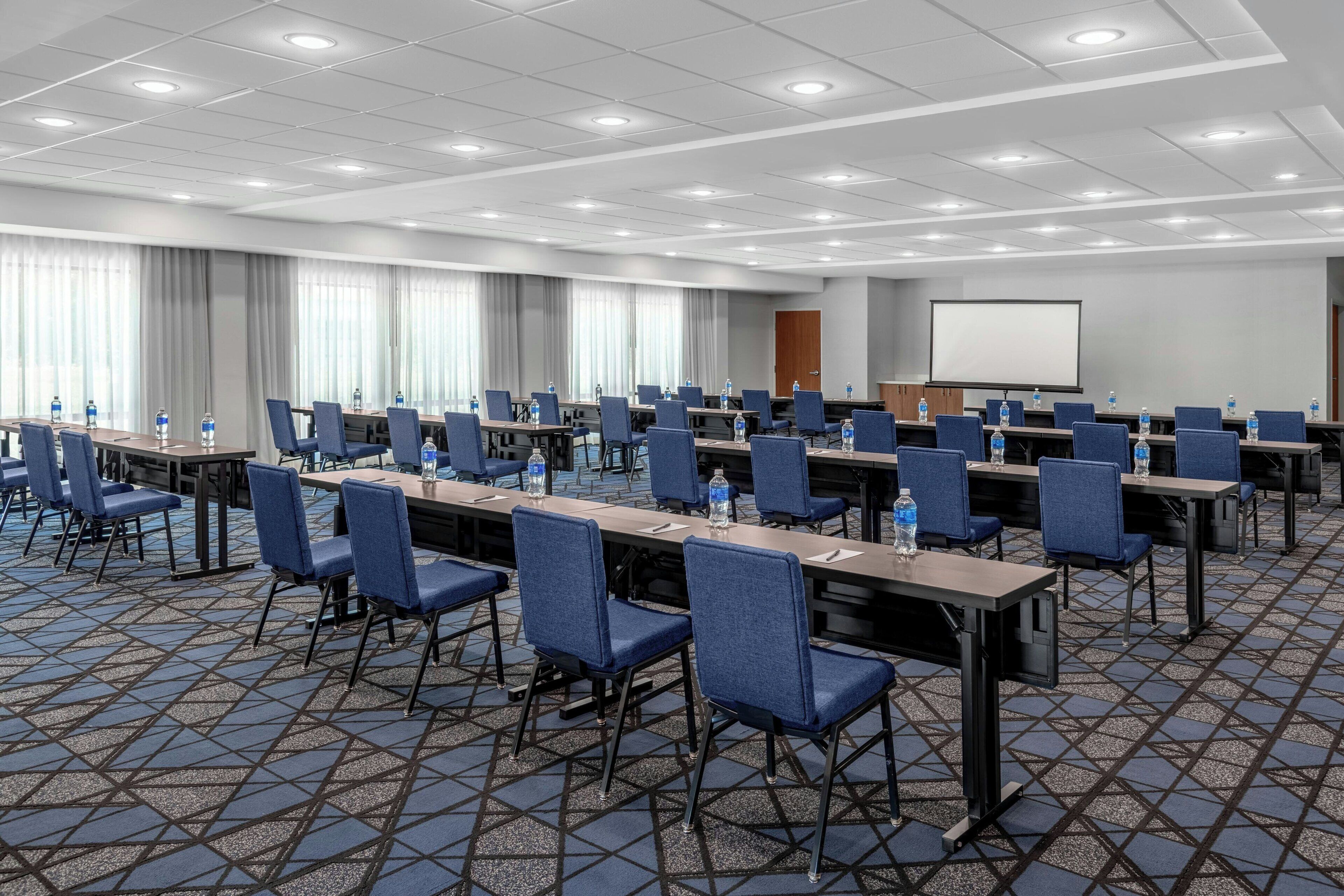 Una sala de conferencias con varias mesas, sillas y una pantalla de proyector.